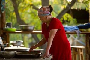 una mujer con un vestido rojo preparando comida en una sartén en Bel-Zhan Yurt Lodge, en Grigor'yevka