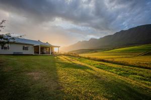 a house in the middle of a field with mountains at Appelsbosch Guest Farm in Swellendam