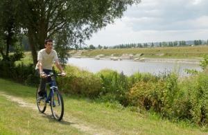 un hombre montando una bicicleta en un camino cerca de un río en Village de Gîtes de l'Anse de Moidrey, en Moidrey