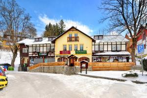 a large yellow building with snow on the ground at Hotel Erika in Špindlerův Mlýn