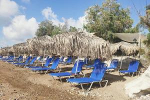 a row of blue chairs on a beach with a straw umbrella at Modern Apartment, Few Meters from the Beach in Néa Koróni