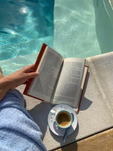 una persona leyendo un libro junto a una piscina con una taza de café en Sa Murta Bianca Guesthouse, en Budoni