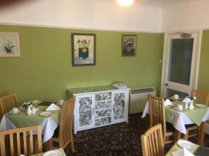 un comedor con 2 mesas y paredes verdes en The Hilary Guesthouse en Llandudno