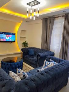 Executive Two & Three Bedroom Suites في ناكورو: غرفة معيشة مع اثنين من الأرائك الزرقاء وتلفزيون