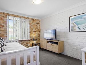 a bedroom with a bed and a tv on a white brick wall at Amersham in Callala Bay