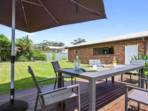 a table and chairs on a deck with an umbrella at Amersham in Callala Bay
