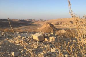 a field with rocks and a mountain in the distance at cozy room in Mitzpe Ramon