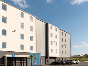 a large white building with cars parked in a parking lot at ibis Budget Cognac in Châteaubernard