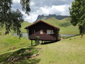 a small wooden house on a hill with a lake at Eland Valley Resort in Underberg
