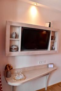 einen Flachbild-TV an einer Wand mit einem Regal in der Unterkunft Gastinger Hotel-Restaurant in Schmiedefeld am Rennsteig