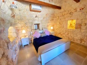 ein Schlafzimmer mit einem Bett und einer Steinmauer in der Unterkunft TRULLO DEL BOSCHETTO in Carovigno