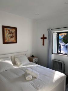 uma cama branca num quarto com uma cruz na parede em Casa do Chinelo Azul em Queluz