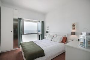 a white bedroom with a bed and a window at Amazing Sesimbra Duplex by the beach in Sesimbra