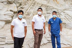 three men wearing face masks stand in front of a statue at Samananchis Machupicchu in Machu Picchu