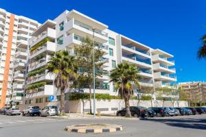 a large white apartment building with palm trees in a parking lot at Praia da Rocha Edifício Foz Palace t2 in Portimão