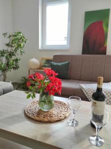 eine Vase mit roten Blumen auf dem Tisch und einer Flasche Wein in der Unterkunft Sea Story Apartment in Igalo