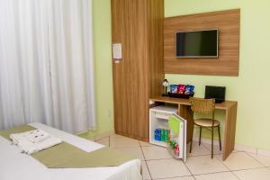 a room with a bed and a desk with a television at Domus Hotel Titânio Canaã dos Carajás in Canaã dos Carajás