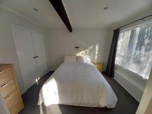 um quarto com uma cama com lençóis brancos e uma janela em Lemon Tree Apartment Tawa em Wellington