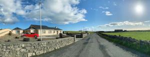 a dirt road with a stone wall and a red car at Glasha Meadows B&B in Doolin