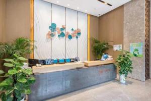 a lobby with a reception desk with plants and a window at Home Plus Hotel in Suzhou