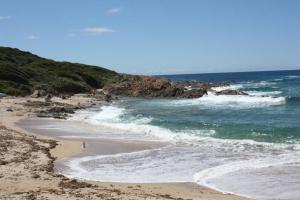 a beach with people walking on the sand and the ocean at Grande maison au cadre verdoyant au centre village in Cargèse +7 photos