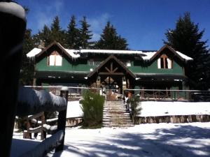 a large green house with snow in front of it at Hostel La Angostura in Villa La Angostura