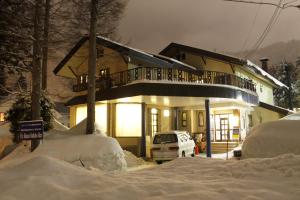 a house in the snow with a car parked in front at K's House Hakuba Alps - Travelers Hostel in Hakuba