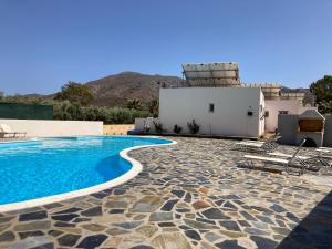 a swimming pool with a house and mountains in the background at Rousolakos Pool Apartments in Palekastron