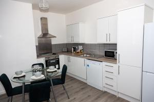 a kitchen with white cabinets and a table and chairs at Alexander Apartments Powdene House in Newcastle upon Tyne