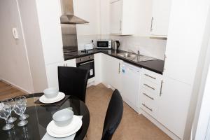 uma cozinha com armários brancos e uma mesa e cadeiras pretas em Alexander Apartments Powdene House em Newcastle upon Tyne