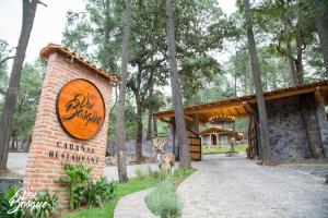 un cerf debout à côté d'un bâtiment en briques avec un panneau dans l'établissement Cabañas La Vid Del Bosque, à Tapalpa