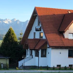 a white house with red roofs with mountains in the background at Velo Apartamenty in Czorsztyn