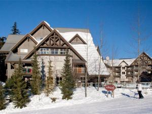 a building in the snow with a person standing in front of it at True Ski in Ski out Condo with hot tub and pool at the Aspens in Whistler
