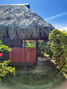 uma cabana com telhado de palha e um portão vermelho em HUAHINE - Bungalow Tiare em Fare