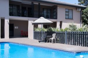 a house with a table and an umbrella next to a pool at Allegro Guesthouse in Bloemfontein