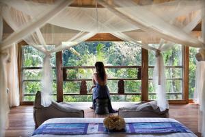 a woman standing in a bedroom looking out the window at Blue Karma Dijiwa Ubud in Ubud