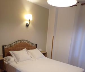 Un dormitorio con una cama blanca con una luz en la pared en Hospedaje Torreón en Cangas de Onís