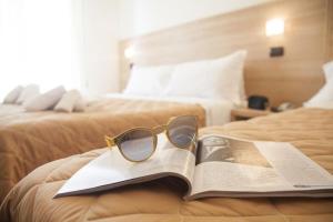 Un par de gafas sentadas encima de un libro en una cama en Hotel Costazzurra by Interlux, en Rímini