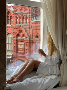 
a woman sitting on a bed in front of a window at Tchaikovsky Hotel in Moscow
