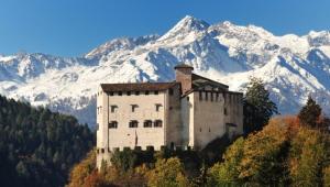 a building on a hill with mountains in the background at Hotel Corona in Pinzolo