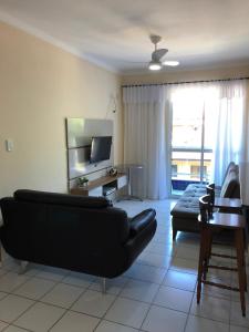 een woonkamer met een zwarte bank en een televisie bij Apartamento em Ubatuba - Praia Grande in Ubatuba