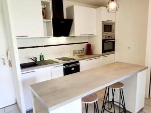 una cucina con mobili bianchi e un bancone con sgabelli di Charmant appartement avec terrasse et jardin au calme Proche Bus Métro a Tolosa