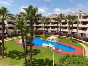 an apartment building with a swimming pool and palm trees at Apartamento en Playa Flamenca (residencial El Rincon) in Playas de Orihuela