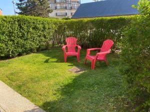 two red chairs sitting in the grass next to a hedge at T2 jardinet, accès direct plage in Cabourg