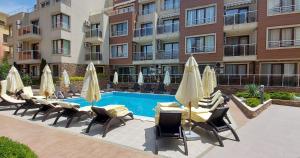 a pool with chairs and umbrellas next to a building at Менада Хоризонт Апартаменти in Sozopol
