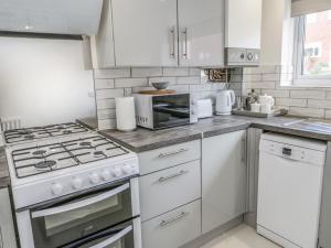 a white kitchen with a stove and a microwave at 22 Gwel Yr Wyddfa in Menai Bridge