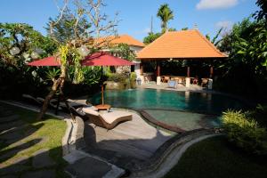 a swimming pool with a bench and an umbrella at Puri Andong Villa in Ubud