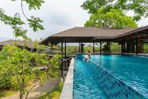 Eine Frau sitzt am Rand eines Swimmingpools in einem Ferienresort. in der Unterkunft Rain Tree Khao Yai Hotel in Phayayen