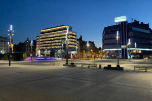 una plaza de la ciudad con bancos y edificios por la noche en Niebieski apartament Teatralna, en Katowice