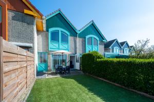 ein Haus mit einem Zaun und einem Tisch mit einem Regenschirm in der Unterkunft Grasse 148 - Kustpark Village Scaldia in Hoofdplaat